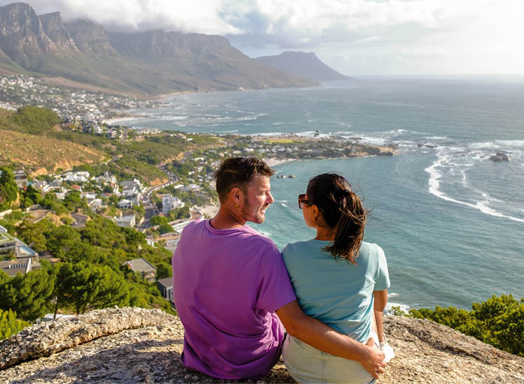 a couple of men and women at The Rock viewpoint in Cape Town over Campsbay, view over Camps Bay with fog over the ocean. fog coming in from the ocean at Camps Bay Cape Town South Africa