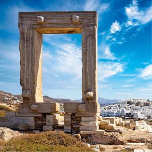 The famous gate of Naxos island, so called Portara from the temple of Apollon, in front of the whitewashed houses of the city, witout people, Cyclades, Greece