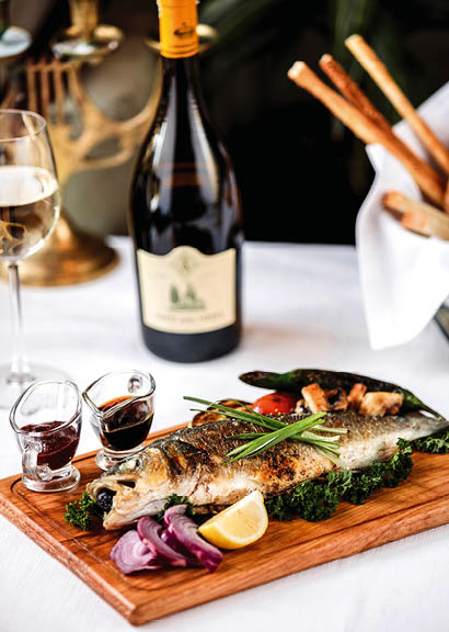 side view of baked sea bass with vegetables red onion and lemon on a wodden board