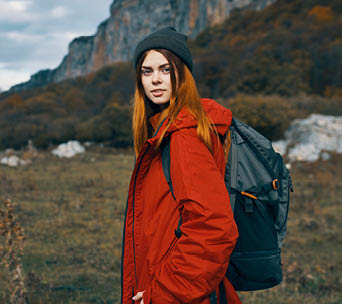 a woman in a red jacket and warm hats walks in a meadow in the mountains in nature. High quality photo