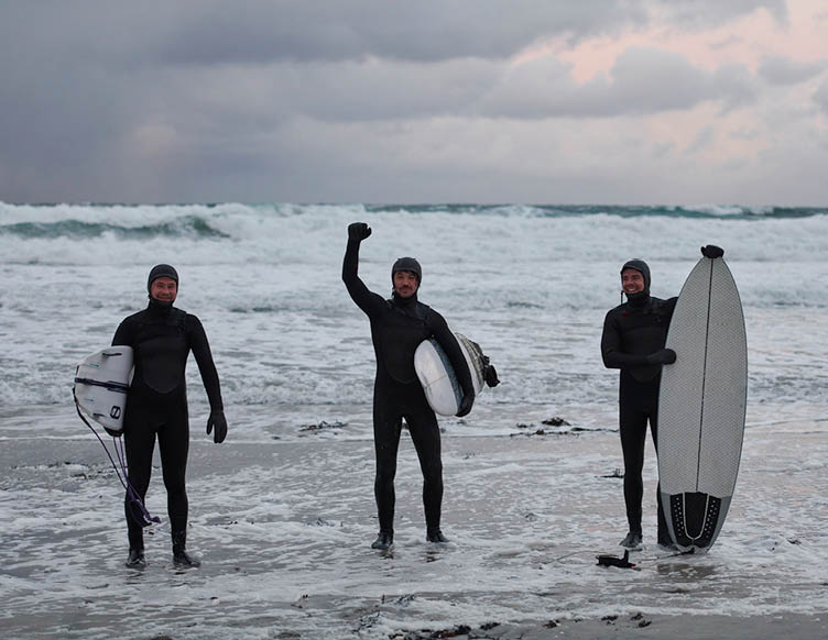Authentic local Arctic surfers going by snowy beach after surfing in Northern sea. Norwegian sea coastline. Winter water activities extreme sport
