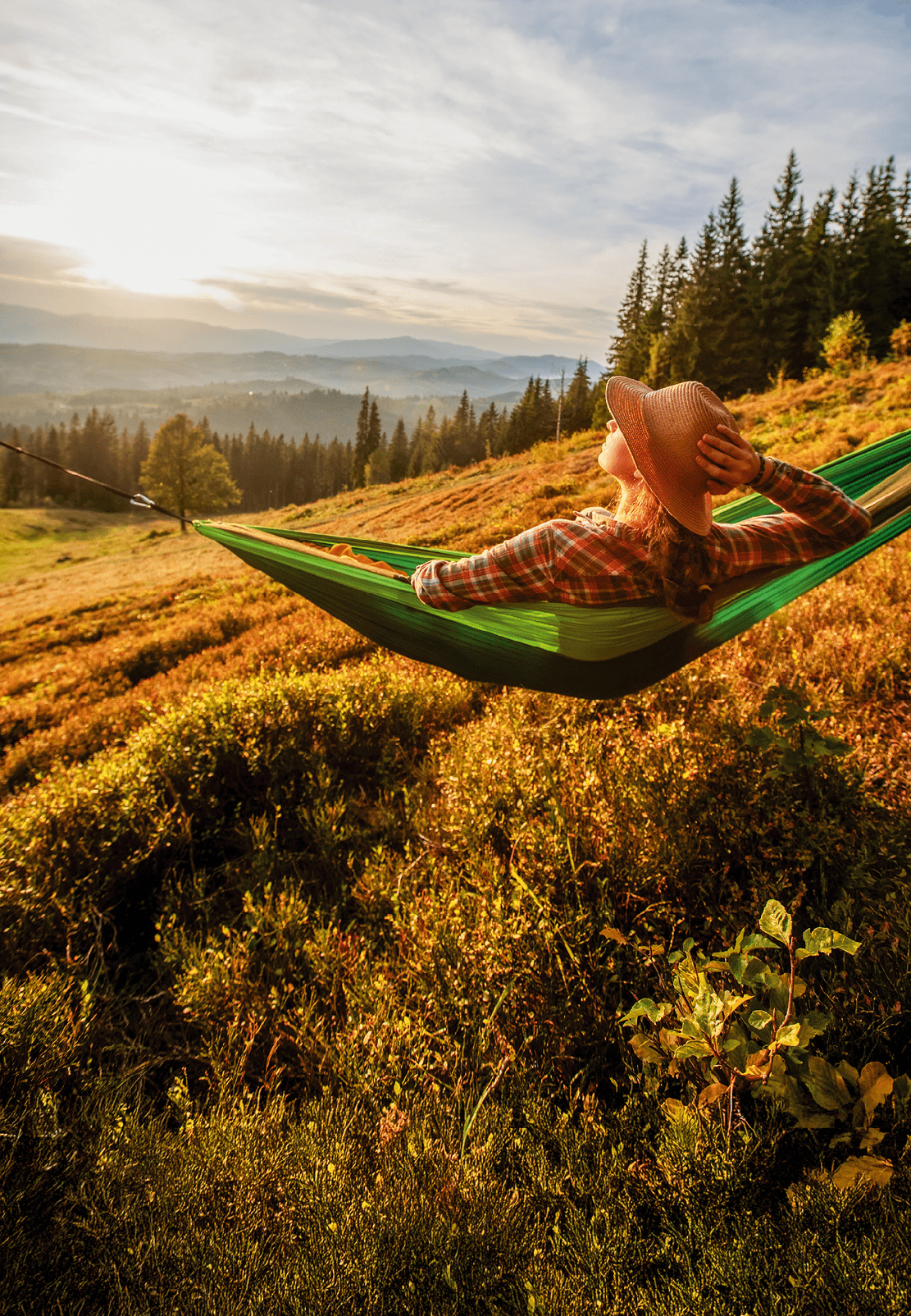 Woman hiker resting after climbing in a hammock at sunset