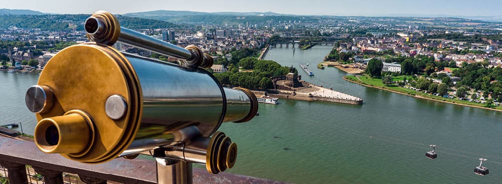 Ein Fernrohr auf einem Aussichtspunkt mit Blick auf die Stadt Koblenz und das Deutsche Eck, eine Hochseilbahn f hrt ber den Fluss bei klarem Himmel.  Deutsches Eck - Koblenz, Germany; Shutterstock ID 721697401 721697401