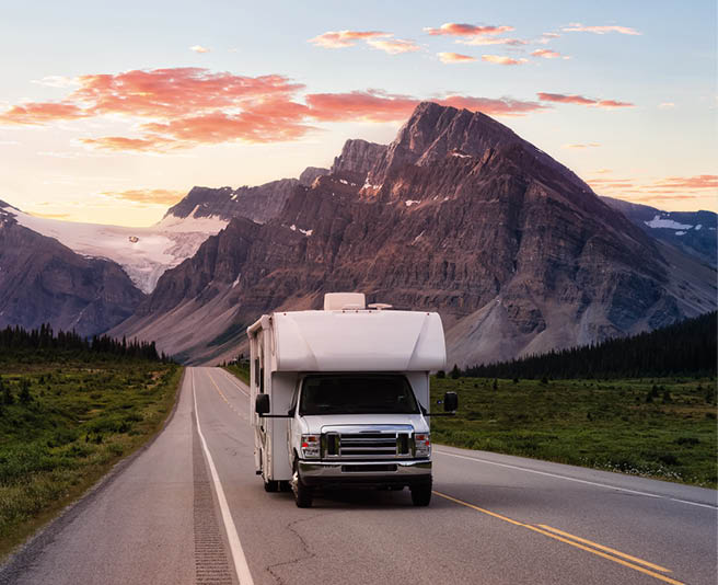 Scenic road in the Canadian Rockies during a vibrant sunny summer sunrise. White RV Driving on route. Taken in Icefields Parkway, Banff National Park, Alberta, Canada.