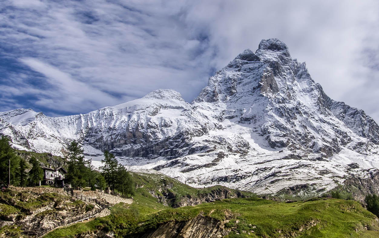 Panoramic view of the south face of the Matterhorn, view from the Breuil-Cervinia village.Green meadow in the front and blue sky with white clouds above mountains. Summer in the Alps, Italy, Europe.