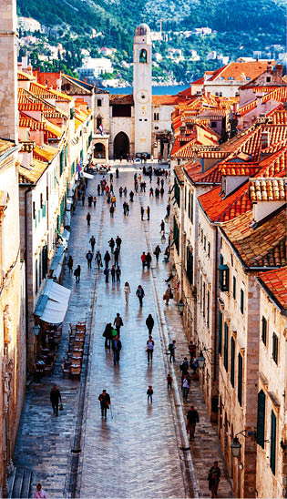 Dubrovnik, Croatia. Aerial view of Old Fortress Dubrovnik in Croatia with Cathedral tower with blue cloudy sky. Famous Stradun street with people