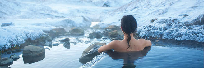 The girl bathes in a hot spring in the open air with a gorgeous view of the snowy mountains. Incredible iceland in winter.