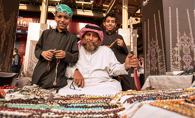 A man and two boys in traditional dress at a masbaha stall