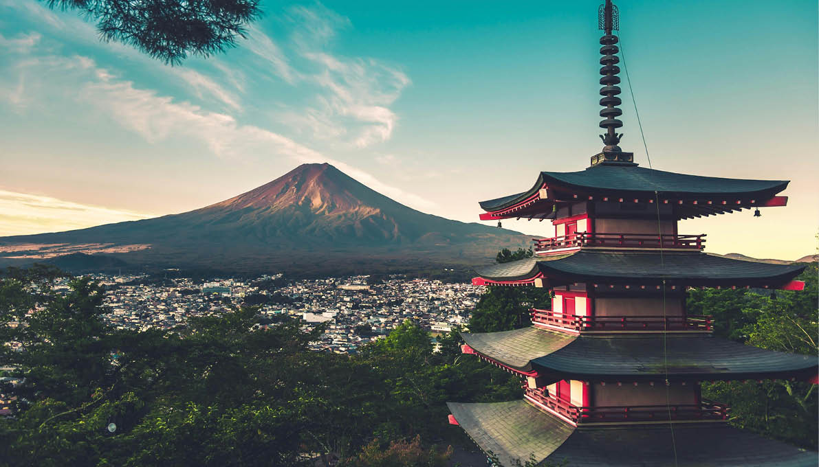 F nfst ckige Pagode inmitten gr ner B ume mit Blick auf eine Stadt und den Fuji in der Abendd mmerung. 