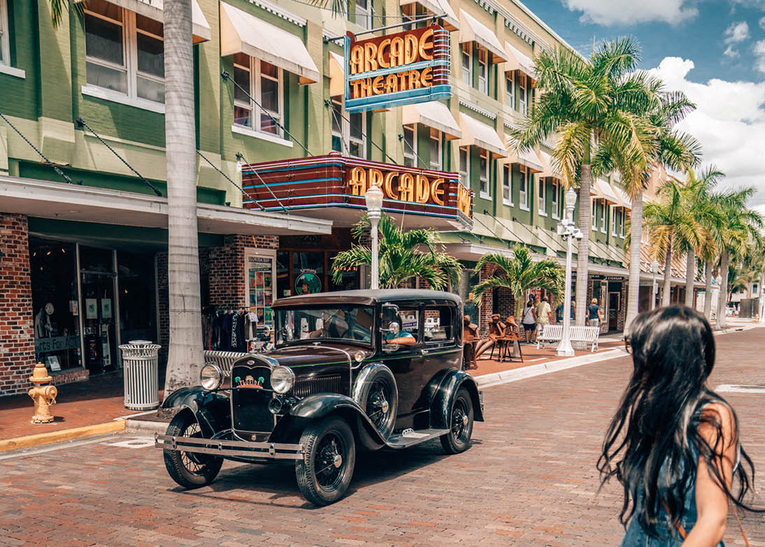 Frau berquert gepflasterte Stra e vor einem historischen Auto und dem Geb ude des Arcade Theatre mit Leuchtreklame.