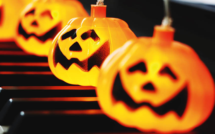 Leuchtende Halloween-K rbislichter mit geschnitzten Gesichtern stehen in Reihe auf schwarzen und roten Tasten eines Klaviers. 