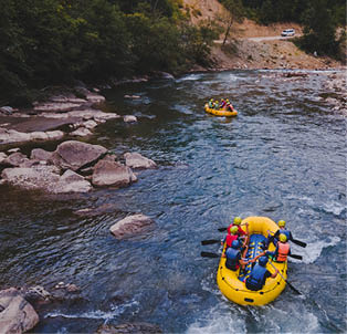 Zwei gelbe Schlauchboote mit Personen in Sicherheitsausr stung beim Rafting auf einem felsigen Gebirgsfluss.