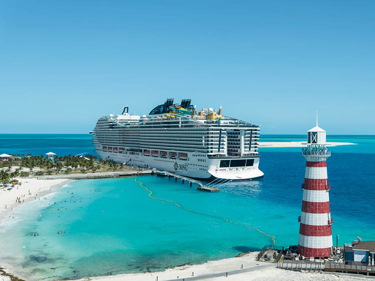Gro es Kreuzfahrtschiff der Reederei MSC liegt vor einer tropischen Insel mit wei em Sandstrand, t rkisblauem Wasser und rot-wei gestreiftem Leuchtturm.