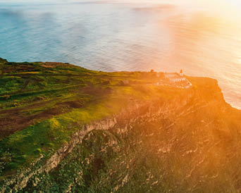 Aerial view of rough ocean with waves, volcanic beach, sunset over a huge cliff in Lighthouse Ponta do Pargo, Madeira, Portugal