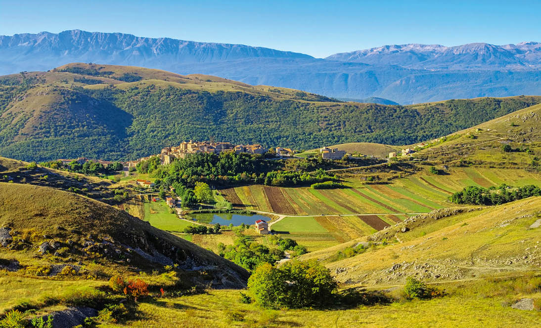 Dorf mit umliegenden Feldern in einem gr nen Tal, umgeben von sanften H geln und Bergen.
