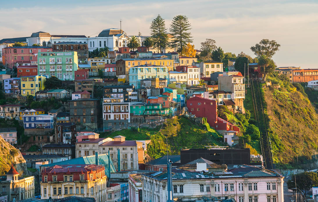 Bunte H user auf einem H gel in Valpara so bei Tageslicht, mit Aufzugsschienen rechts und Stadt im Hintergrund.