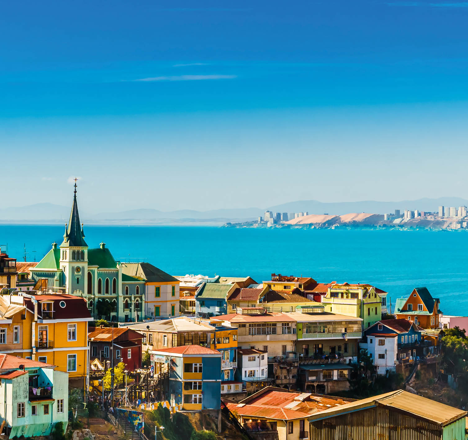 Blick ber bunte H user und eine Kirche auf blauen Ozean mit Hochh usern und H geln im Hintergrund.