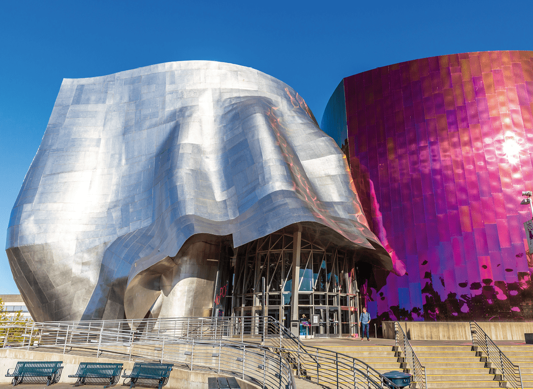 Moderne Geb udefassade mit geschwungenen silbernen und pinkfarbenen Metallfl chen unter blauem Himmel.