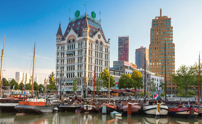 Historisches Geb ude mit Uhrturm am Hafen, davor Segelboote und moderne Hochh user im Hintergrund.