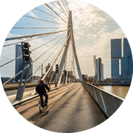 Radfahrer auf Br cke mit schr gen Seilen, im Hintergrund moderne Hochh user am Wasser.