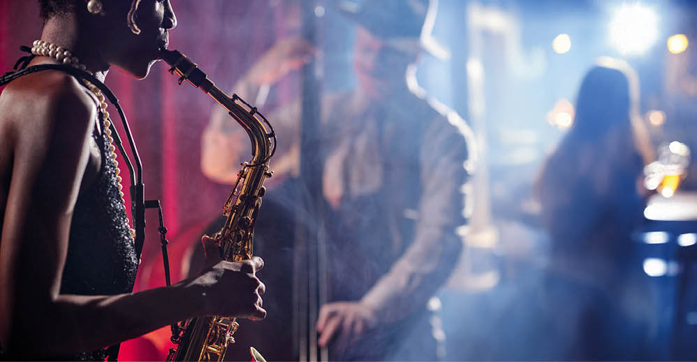 Junge afroamerikanische Frau spielt Saxophon mit Jazzmusikern live auf der B hne