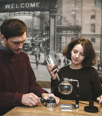 Vintage couple preparing coffee with vacuum coffee maker.Coffee shop. Vintage toned
