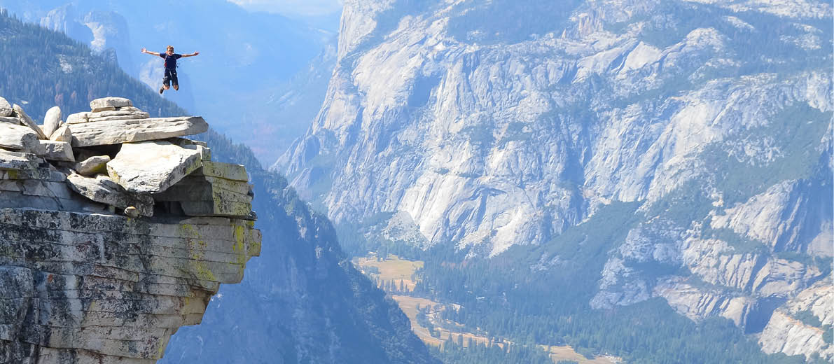 A vertical shot of a person jumping on a cliff at Half Dome, Yosemite, California