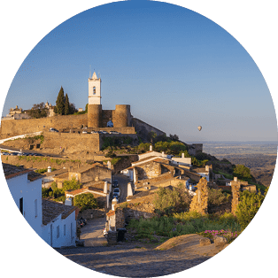 Wei e H user und Burganlage auf einem H gel, dar ber mehrere bunte Hei luftballons vor weiter Ebene.