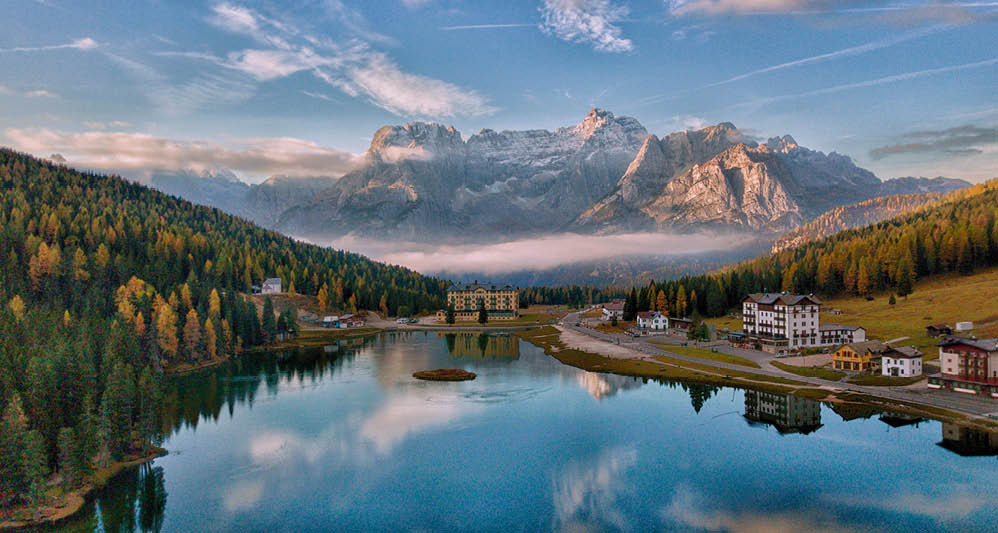 Bergsee mit umliegenden W ldern und Bergmassiv im Hintergrund bei Sonnenaufgang