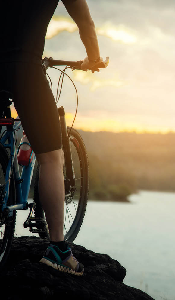 Mann mit Fahrrad auf Felsvorsprung am See bei Sonnenuntergang