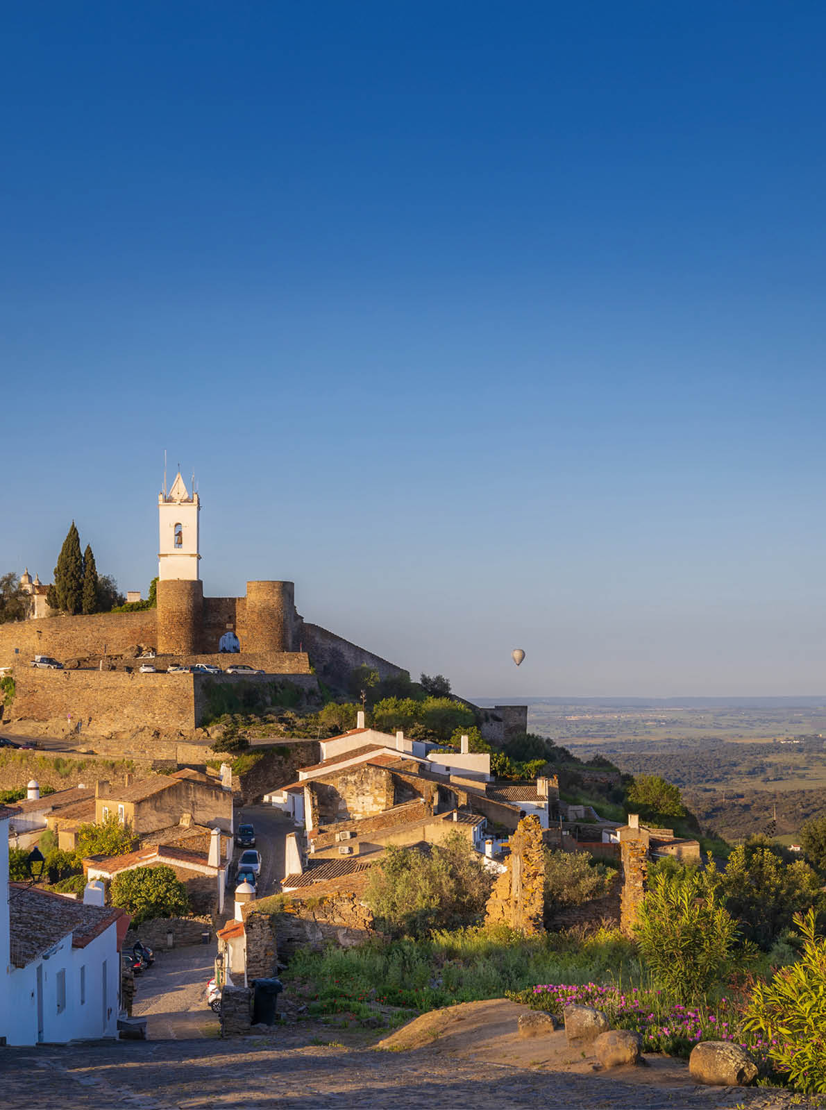 Wei e H user und Burganlage auf einem H gel, dar ber mehrere bunte Hei luftballons vor weiter Ebene.