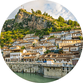 Dicht bebaute Hanglage mit traditionellen wei en H usern vor bewaldetem H gel und Felsen mit Fahne.