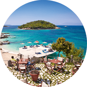 Terrassenrestaurant mit Holzm beln ber Strand und t rkisfarbenem Wasser, kleine Insel im Hintergrund.