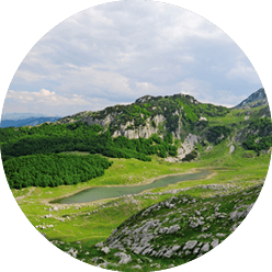 Felsige H gellandschaft mit gr nen W ldern und kleinem Bergsee, umgeben von hohen Bergen.